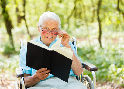 Elderly woman in wheelchair holding and reading a book.